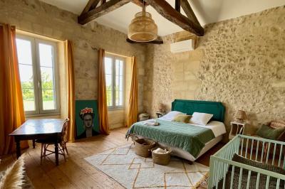 Façade d'une maison en pierre avec terrasse ensoleillée, chaises longues et pots de fleurs sur un sol pavé clair.