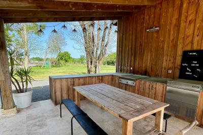 Façade d'une maison en pierre avec terrasse ensoleillée, chaises longues et pots de fleurs sur un sol pavé clair.