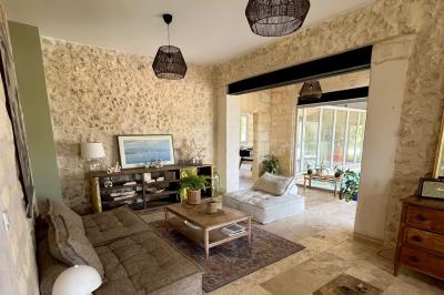 Façade d'une maison en pierre avec terrasse ensoleillée, chaises longues et pots de fleurs sur un sol pavé clair.