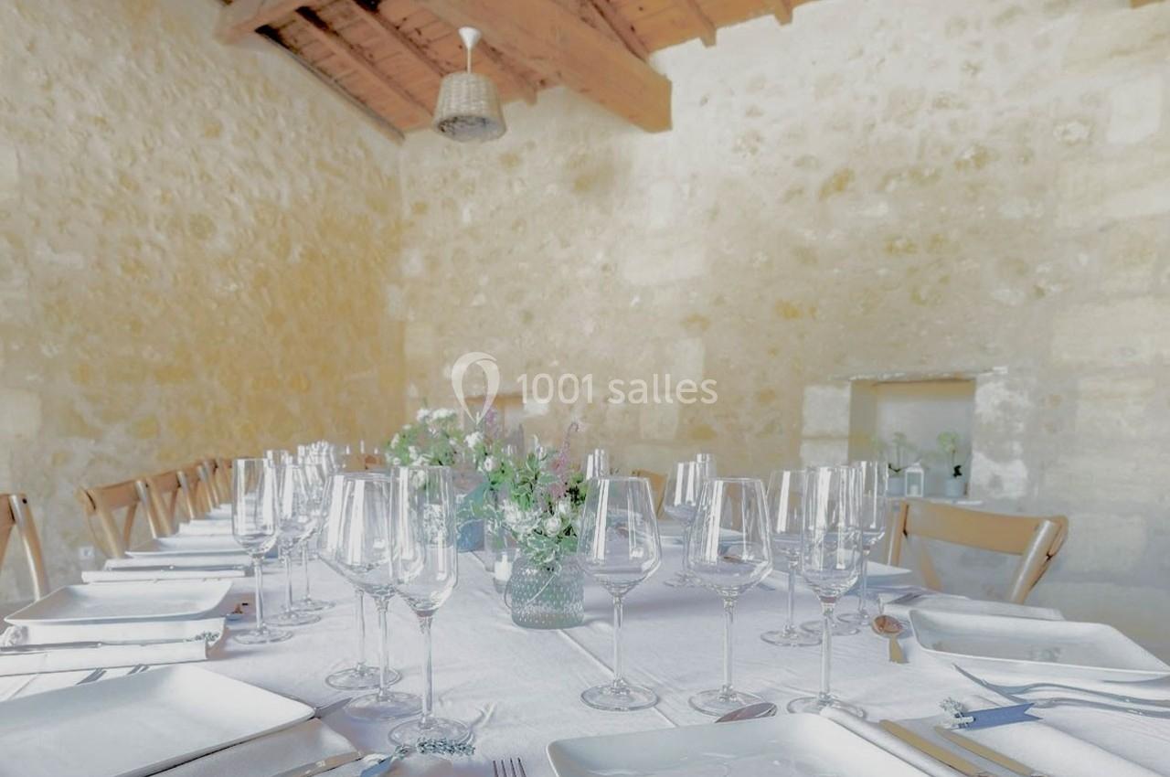 Table dressée avec nappes blanches, vaisselle élégante et bouquets de fleurs, dans une salle aux murs en pierre.