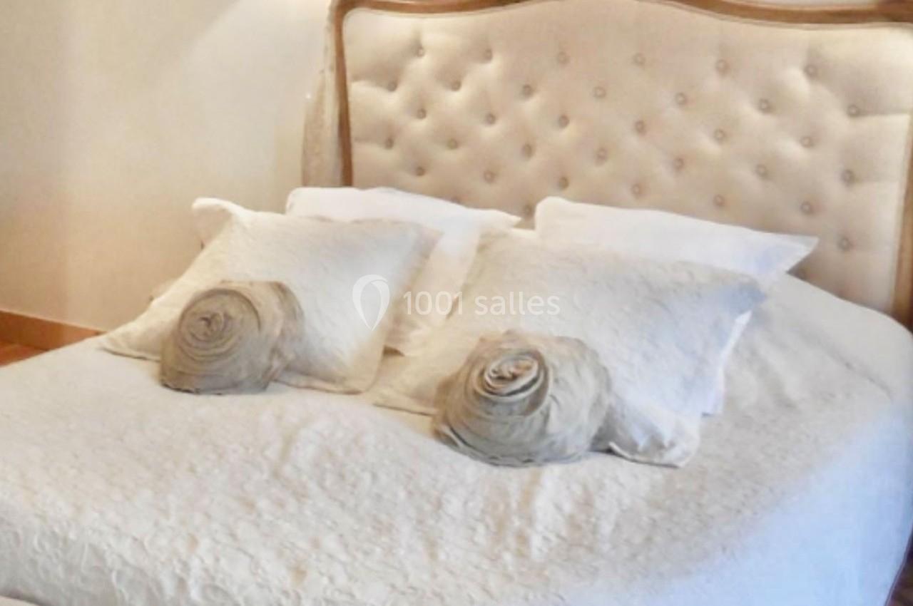 Lit double avec tête de lit capitonnée beige, draps blancs et coussins décoratifs en forme de roses.