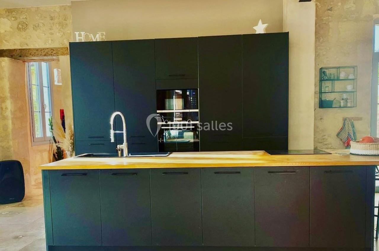 Cuisine moderne avec meubles noirs, plan de travail en bois clair, évier inox et mur en pierre apparente.