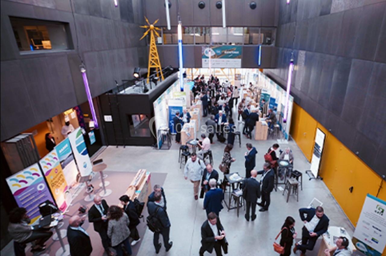 Vue plongeante sur un espace d'exposition intérieur avec des stands, des visiteurs et une ambiance professionnelle.