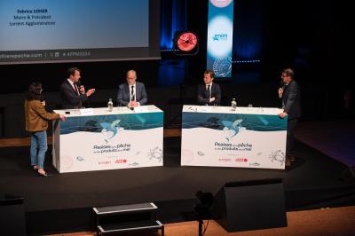 Miniature Agence Ilago #4 Des personnes échangent dans un espace d'exposition intérieur avec des stands et une structure métallique visible en arrière…