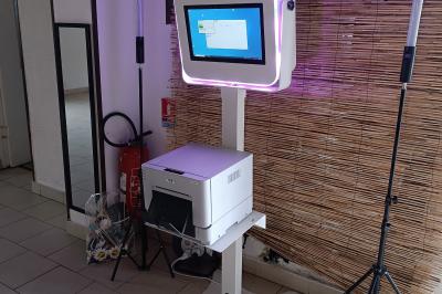 Borne photo sur trépied avec anneaux lumineux, installée dans une salle en briques avec tonneaux en arrière-plan.