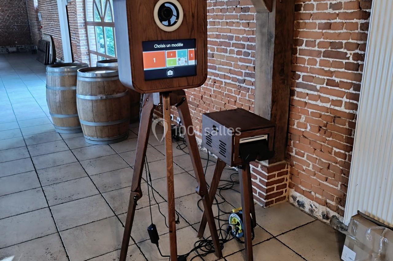 Borne photo en bois sur trépied avec écran tactile et anneau lumineux, installée dans une salle en briques.