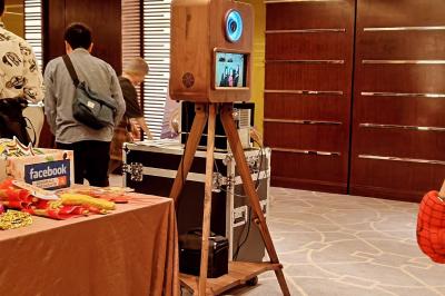 Borne photo sur trépied avec anneaux lumineux, installée dans une salle en briques avec tonneaux en arrière-plan.