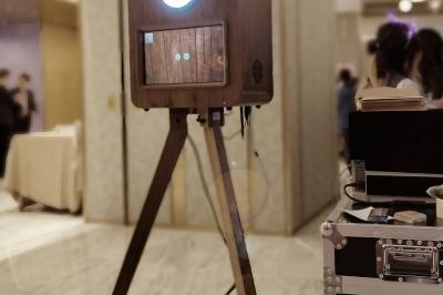 Borne photo sur trépied avec anneaux lumineux, installée dans une salle en briques avec tonneaux en arrière-plan.