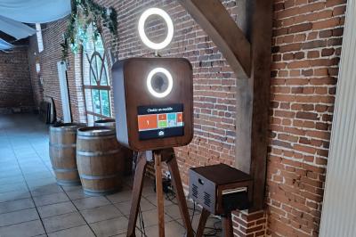 Borne photo en bois sur trépied avec un anneau lumineux allumé, installée dans un espace intérieur.
