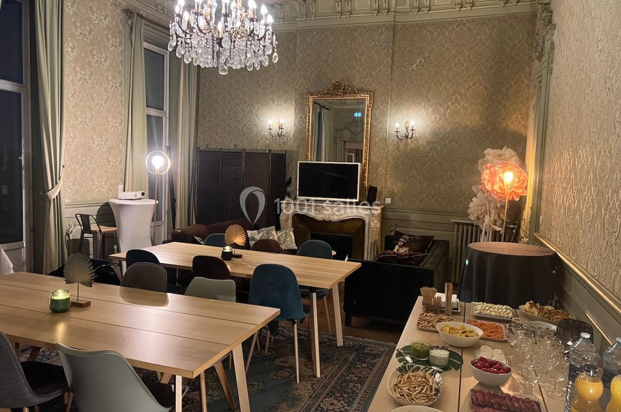 Salle élégante avec tables en bois, chaises colorées, buffet de snacks et boissons, lustre et décoration raffinée.