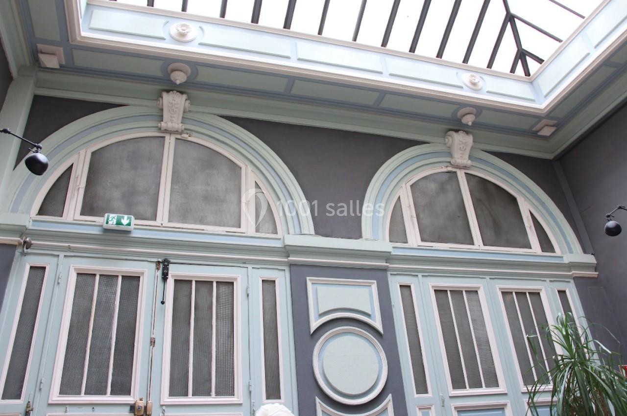 Grande verrière éclairant un intérieur avec des arches et des portes vitrées encadrées de moulures bleues.