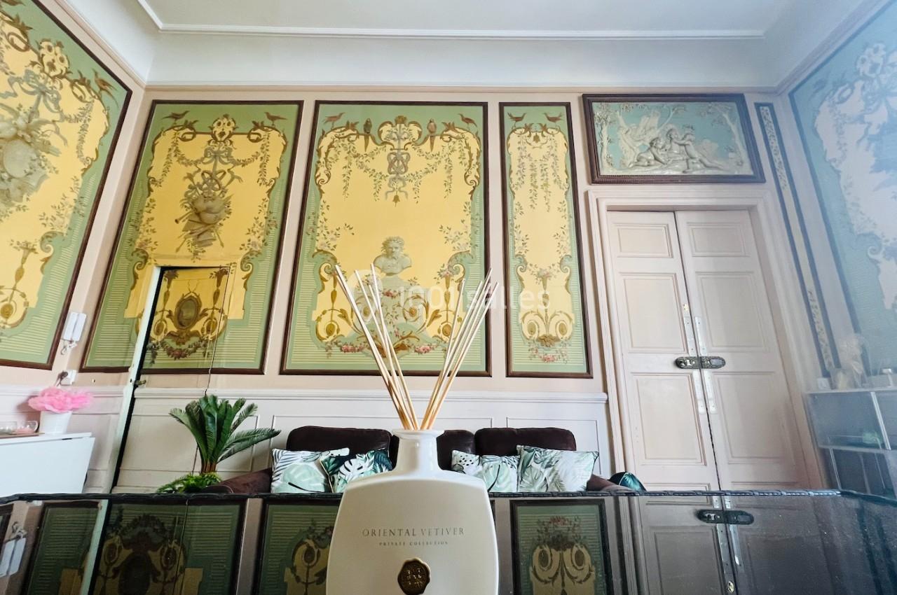 Bouteille de diffuseur de parfum posée sur une table en verre, dans un salon décoré de peintures murales classiques.