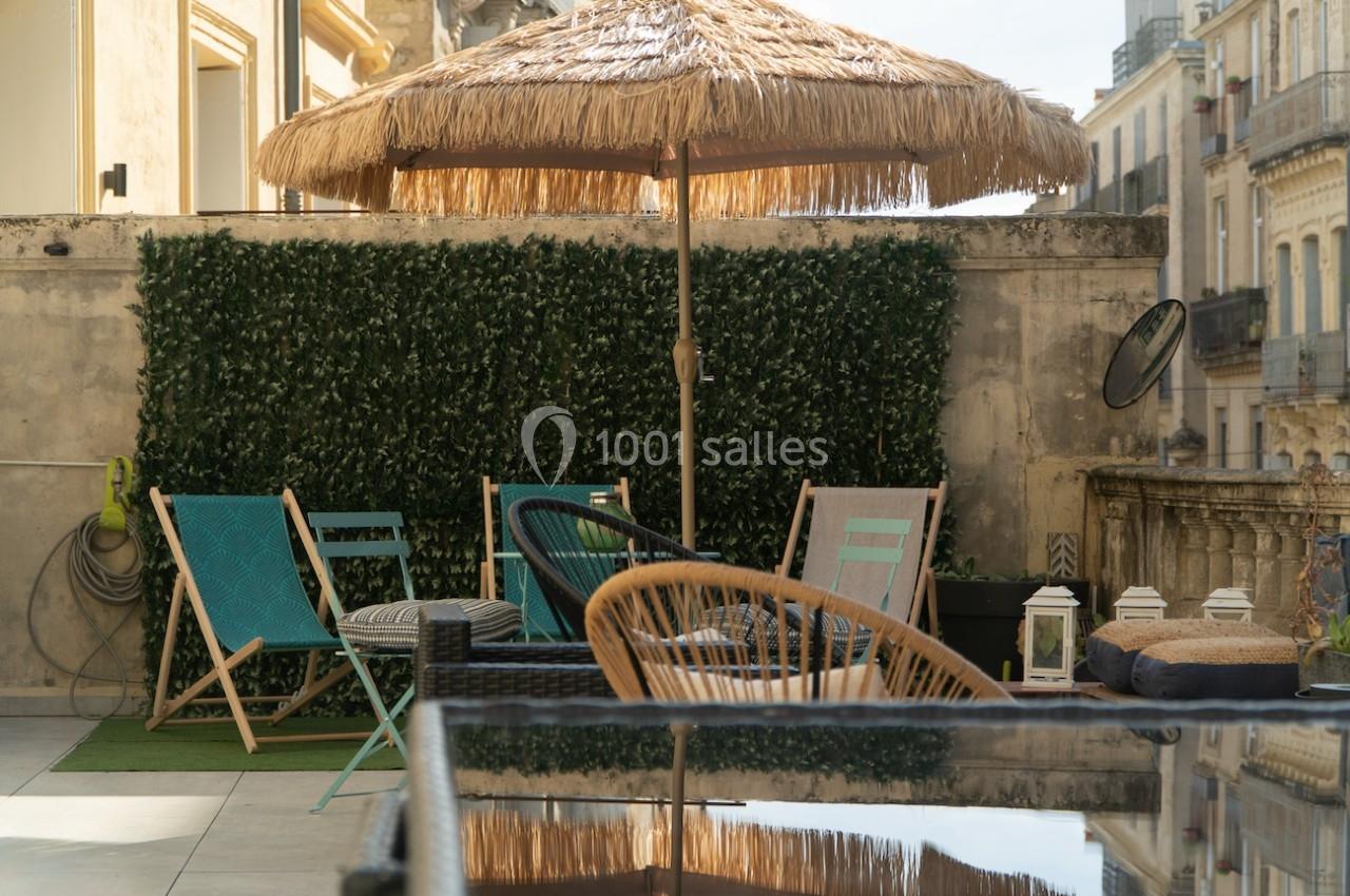 Terrasse aménagée avec des chaises, une table, un parasol en paille et un mur végétal, en milieu urbain.