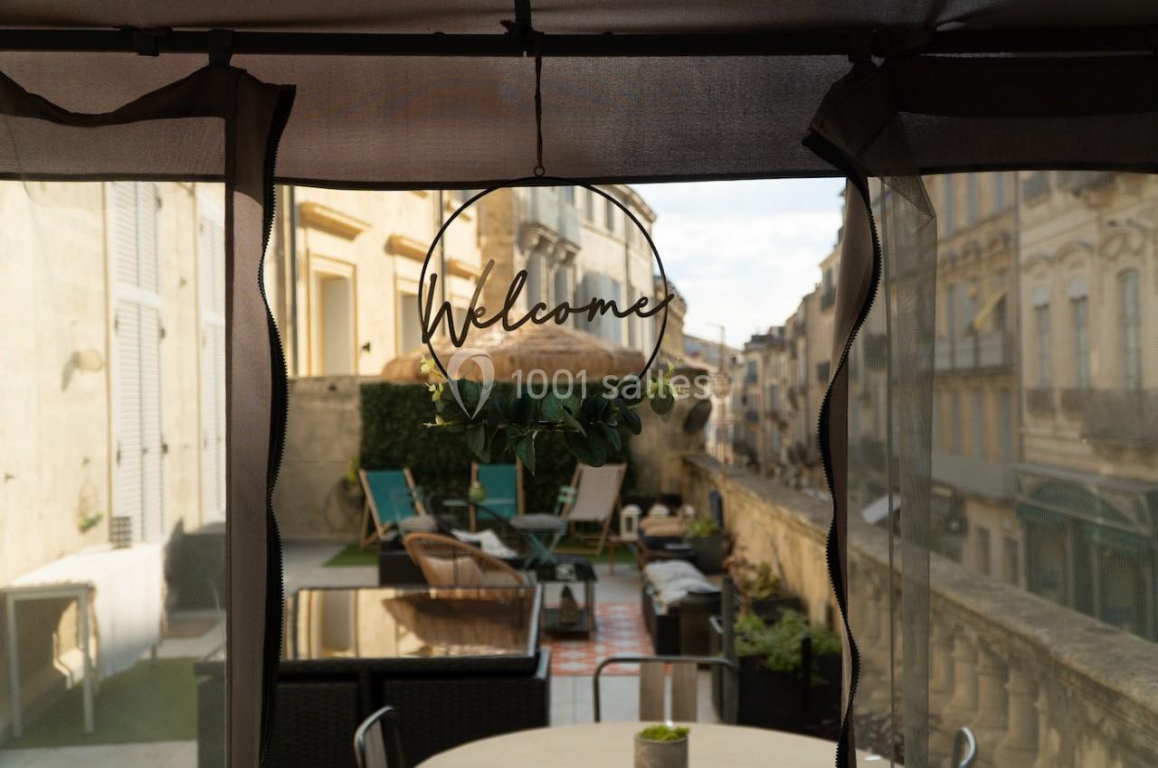 Vue d'une terrasse aménagée avec des fauteuils et une table, encadrée par un panneau ’Welcome’ suspendu.