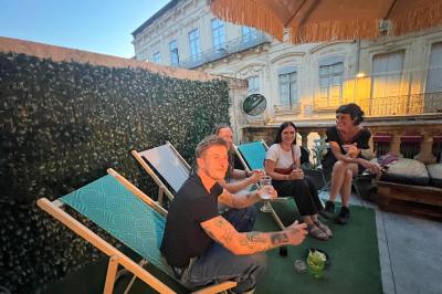 Groupe de personnes discutant et partageant un moment convivial sur une terrasse en soirée, avec des immeubles en arrière…
