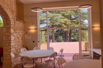 Façade d'un bâtiment en pierre avec de grandes fenêtres, une entrée vitrée et une cour en gravier sous un ciel bleu.