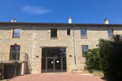 Façade d'un bâtiment en pierre avec de grandes fenêtres, une entrée vitrée et une cour en gravier sous un ciel bleu.