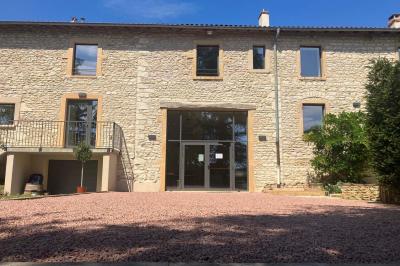 Façade d'un bâtiment en pierre avec de grandes fenêtres, une entrée vitrée et une cour en gravier sous un ciel bleu.