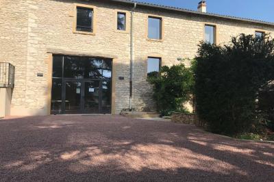 Façade d'un bâtiment en pierre avec de grandes fenêtres, une entrée vitrée et une cour en gravier sous un ciel bleu.