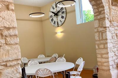 Façade d'un bâtiment en pierre avec de grandes fenêtres, une entrée vitrée et une cour en gravier sous un ciel bleu.