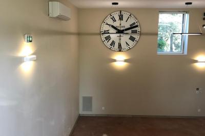 Façade d'un bâtiment en pierre avec de grandes fenêtres, une entrée vitrée et une cour en gravier sous un ciel bleu.