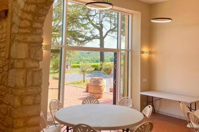 Façade d'un bâtiment en pierre avec de grandes fenêtres, une entrée vitrée et une cour en gravier sous un ciel bleu.