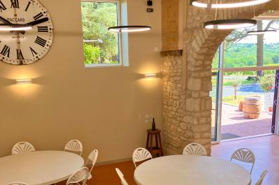 Façade d'un bâtiment en pierre avec de grandes fenêtres, une entrée vitrée et une cour en gravier sous un ciel bleu.