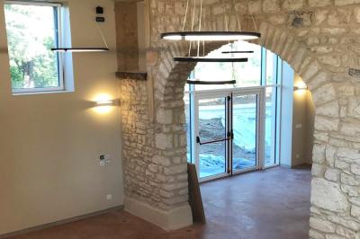 Façade d'un bâtiment en pierre avec de grandes fenêtres, une entrée vitrée et une cour en gravier sous un ciel bleu.