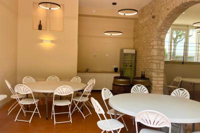 Façade d'un bâtiment en pierre avec de grandes fenêtres, une entrée vitrée et une cour en gravier sous un ciel bleu.