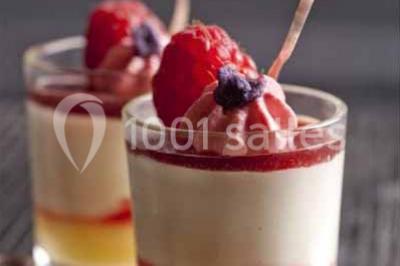 Glycine en fleurs grimpant sur une pergola, avec une maison en briques et des arbustes en arrière-plan.