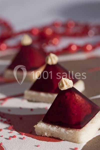 Pyramides de gelée rouge sur des bases de biscuit, décorées de crème et entourées de perles rouges.