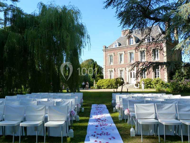Allée centrale décorée de pétales de rose, entourée de chaises blanches, menant à un manoir en pierre dans un jardin.