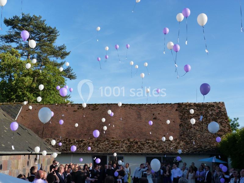Des ballons blancs et violets s'élèvent dans le ciel lors d'un rassemblement en plein air devant un bâtiment en briques.