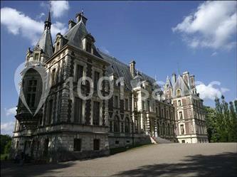 Château historique en pierre avec des tours et des toits en ardoise, entouré d'arbres sous un ciel bleu.