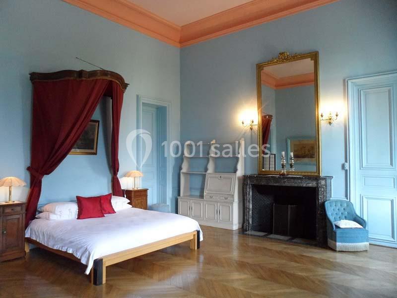 Chambre lumineuse avec lit à baldaquin, cheminée, miroir doré et mobilier classique dans un décor aux tons bleus et bois.