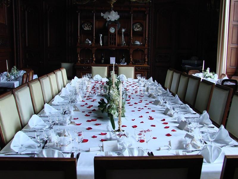 Table élégamment dressée avec nappes blanches, pétales de rose rouges et vaisselle raffinée dans une salle boisée.