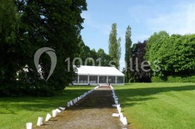 Allée bordée de sacs blancs menant à une tente blanche dans un parc verdoyant par temps ensoleillé.