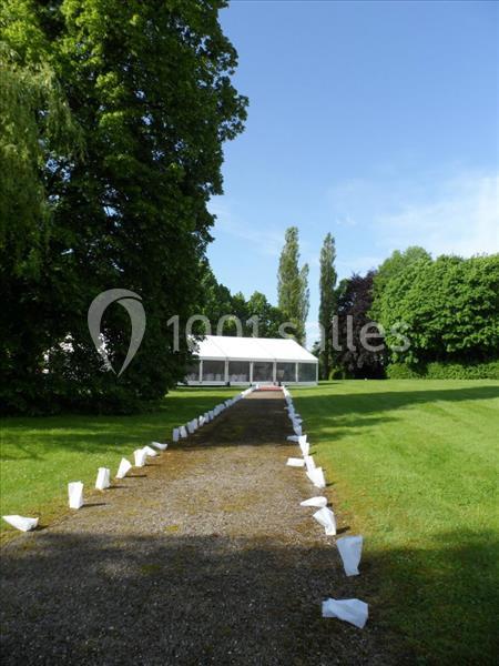Allée bordée de sacs blancs menant à une tente blanche dans un parc verdoyant par temps ensoleillé.