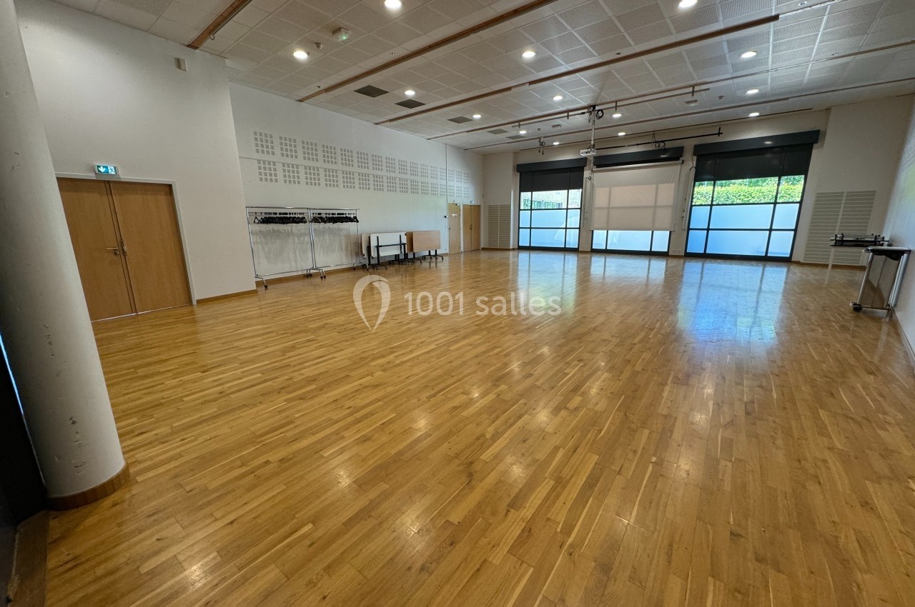 Salle spacieuse avec parquet en bois, murs clairs, grandes fenêtres et portants pour vêtements alignés sur le côté.
