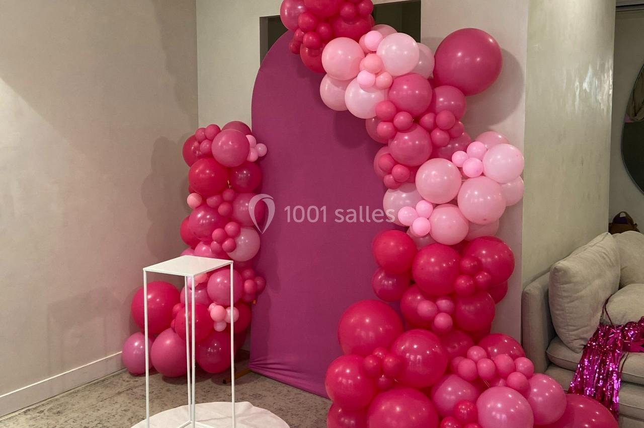 Décoration composée d'arche de ballons roses et fuchsia autour d'un fond rose, avec un support blanc au premier plan.