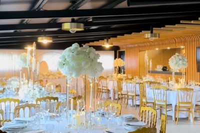 Salle de réception élégante avec tables rondes décorées de nappes blanches, chaises dorées et centres de table fleuris.