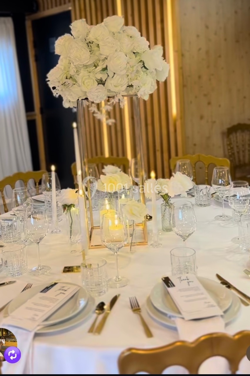 Table de réception élégamment dressée avec nappes blanches, chandeliers, verres et centre de table floral blanc.