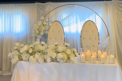 Salle de réception élégante avec tables rondes décorées de nappes blanches, chaises dorées et centres de table fleuris.