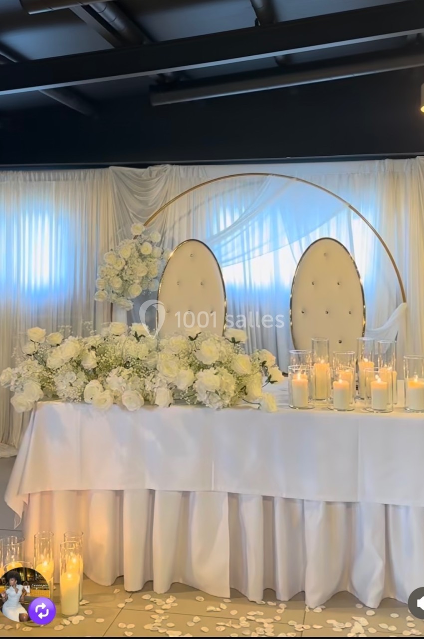 Table décorée pour un mariage avec des fleurs blanches, des bougies et deux chaises ovales devant un rideau clair.