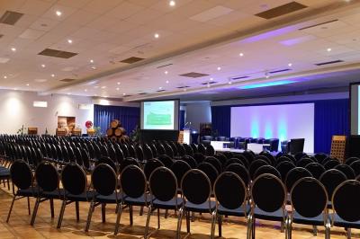 Un couloir d'exposition avec stands éclairés, affiches, et équipements audio sous un plafond voûté en bois.