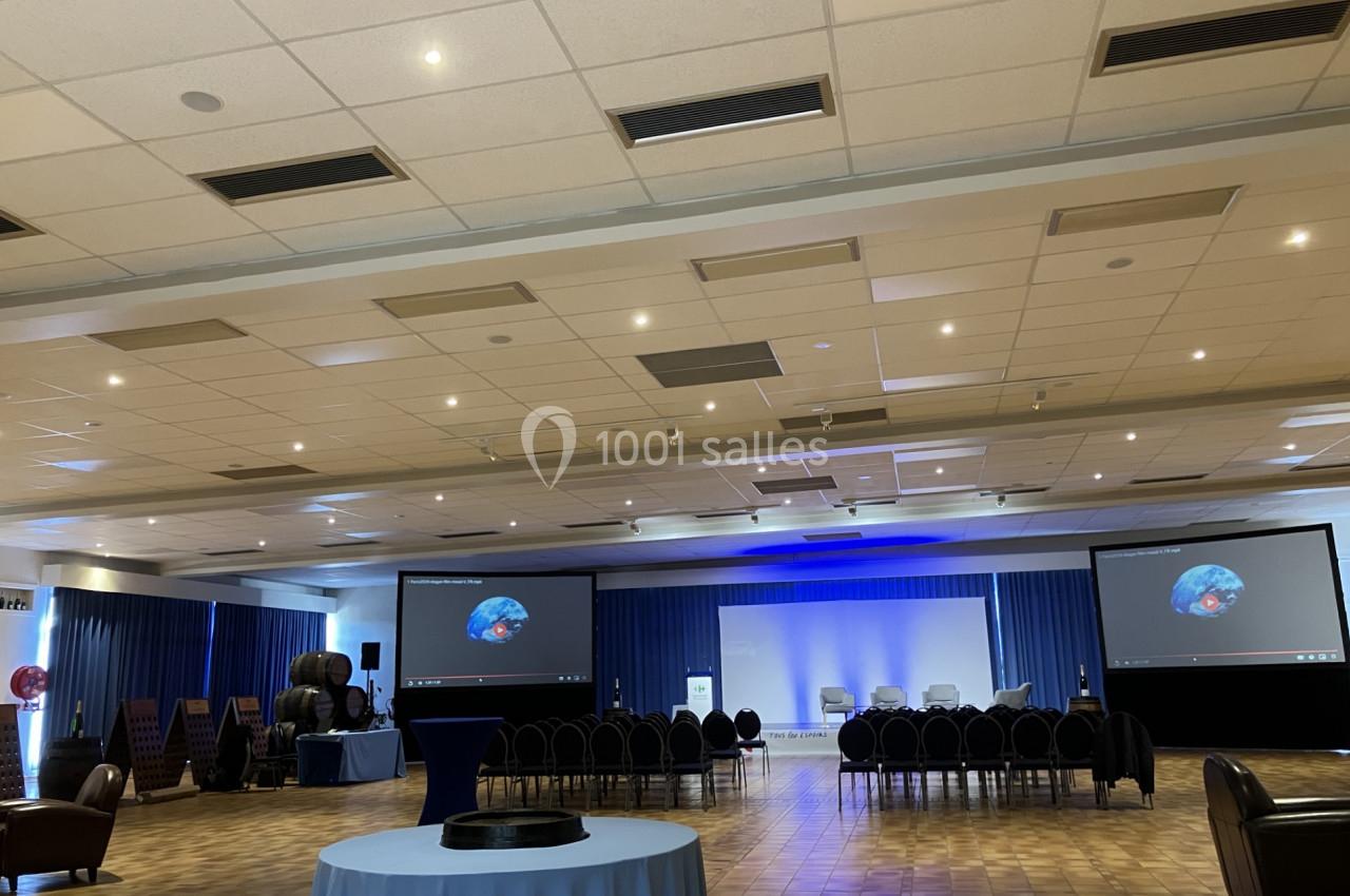 Salle de conférence avec des rangées de chaises, deux écrans projetant une image et un éclairage bleu au fond.
