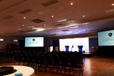 Un couloir d'exposition avec stands éclairés, affiches, et équipements audio sous un plafond voûté en bois.