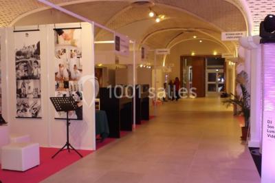 Un couloir d'exposition avec stands éclairés, affiches, et équipements audio sous un plafond voûté en bois.