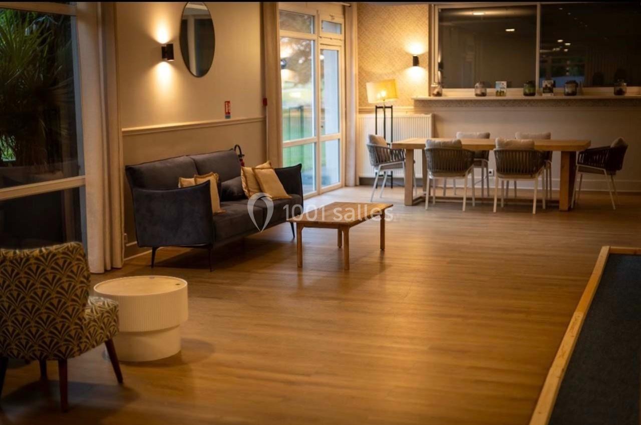 Espace intérieur lumineux avec canapé, table basse, table à manger et grandes fenêtres donnant sur l'extérieur.