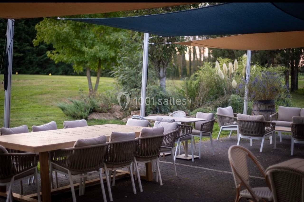 Terrasse extérieure avec tables et chaises en rotin sous des voiles d'ombrage, entourée de verdure.